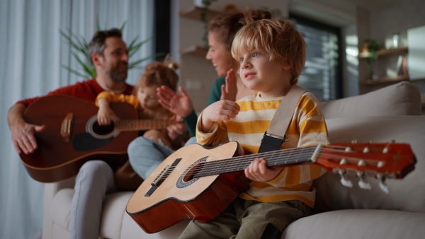 Little children with parents playing the guitar on a sofa at home.