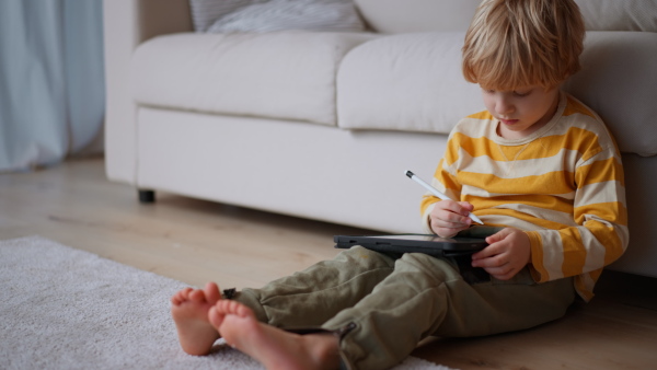 A little boy sitting on floor and using tablet at home