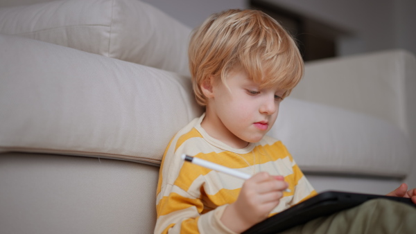 A little boy lying on floor and using tablet at home