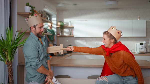 Funny young parents in knights costumes playing with diy swords at home