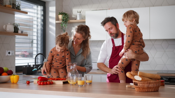 A happy young family with little children cooking together at home.