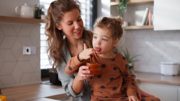 A happy young mother with little daughter in kitchen eating together at home.