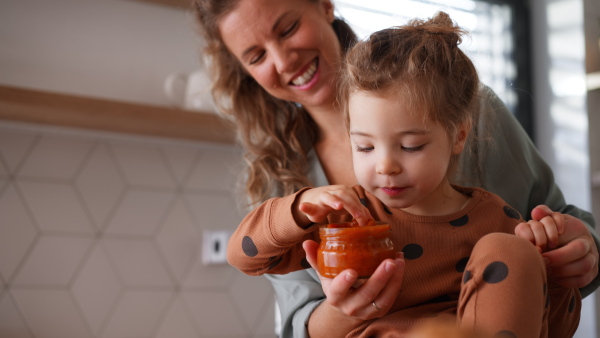 A happy young mother with little daughter in kitchen eating together at home.