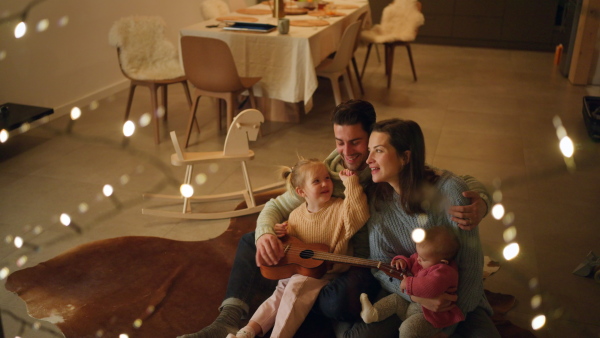 A happy young family with small children sitting on floor and playing the guitar in cabin on holiday.