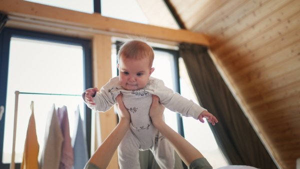 An unrecognizable mother lifting her baby daughter at home.