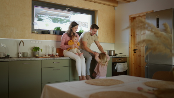 A happy young family with small children sitting together on kitchen counter.