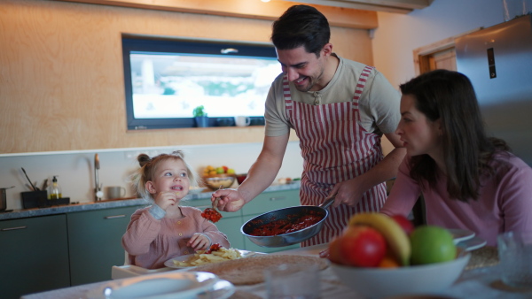 A happy young family with small child eating dinner together in cabin on holiday.