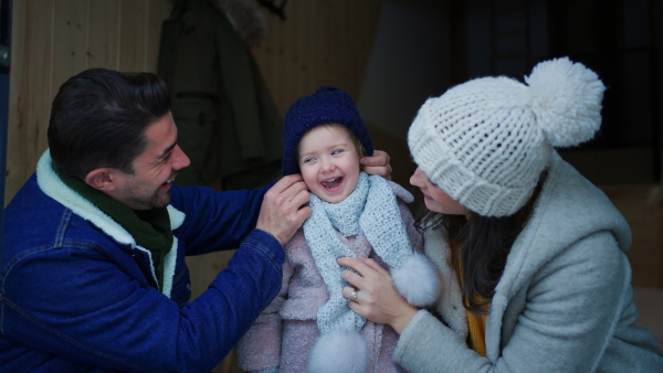 A happy young family on winter holiday in cabin with small child outdoors in snowy nature, looking at camera.