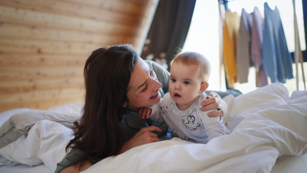 A happy young mother lying on bed and kissing her baby daughter at home.