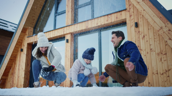 A happy young family on winter holiday in cabin with small child outdoors in snowy nature, snowfighting.