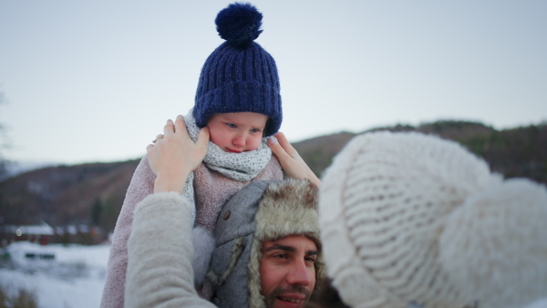 A happy young family on winter holiday with small child outdoors in snowy nature.