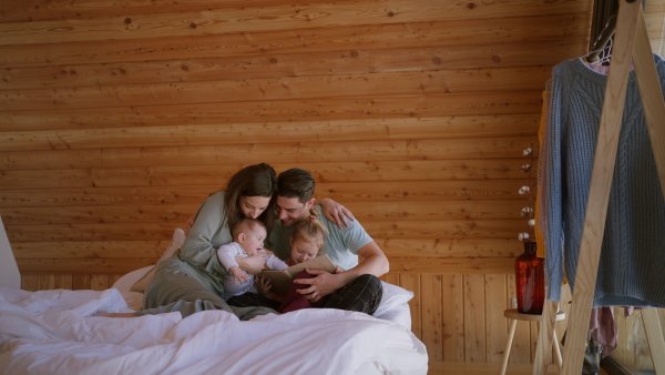 A happy young family with small children reading book on bed at home.