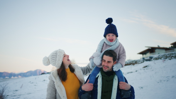 A happy young family on winter holiday with small child outdoors in snowy nature.