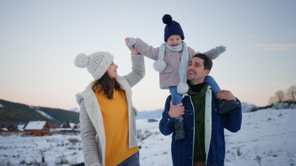 A happy young family on winter holiday with small child outdoors in snowy nature.