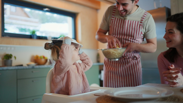 A happy young family with small child eating dinner together in cabin on holiday.