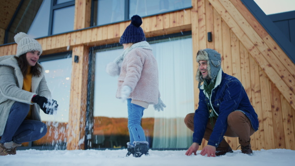 A happy young family on winter holiday in cabin with small child outdoors in snowy nature, snowfighting.