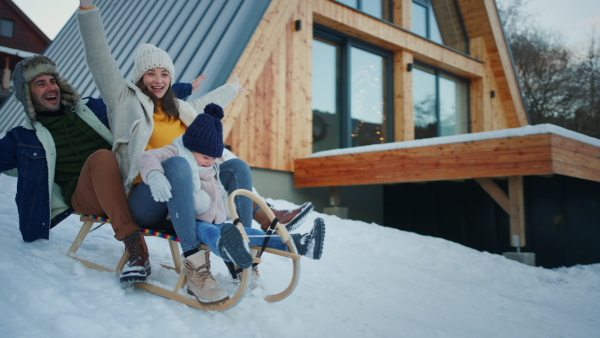 A happy young family on winter holiday with small child sledding outdoors in snowy nature.