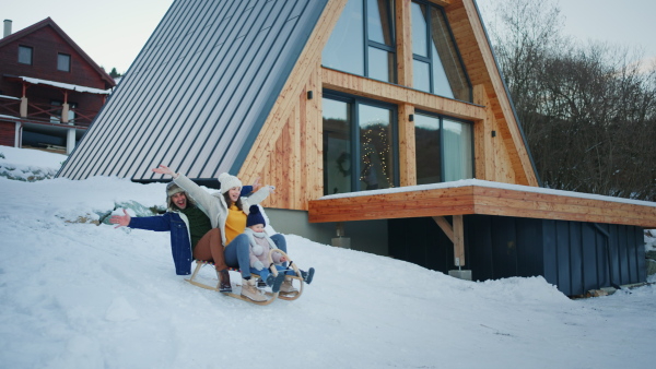 A happy young family on winter holiday with small child sledding outdoors in snowy nature.