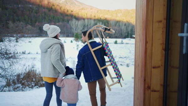 A rear view of young family on winter holiday with small child and sledge outdoors in snowy nature.