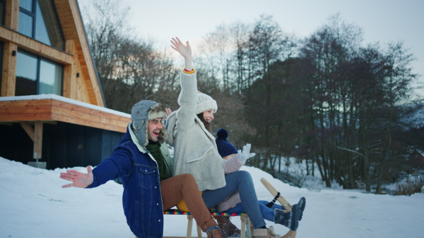 A happy young family on winter holiday with small child sledding outdoors in snowy nature.