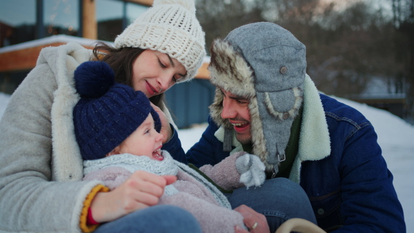 A happy young family on winter holiday with small child kissing outdoors in snowy nature.