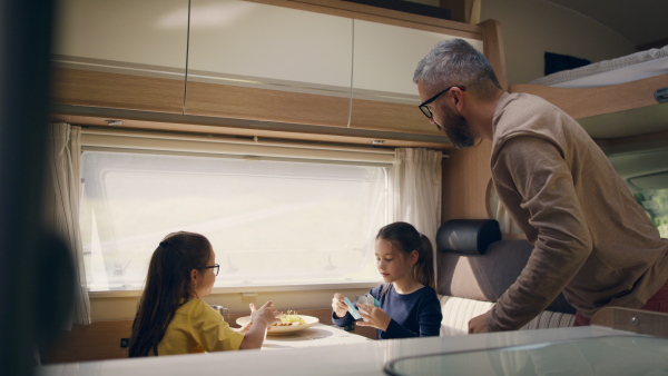 Happy small girls playing cards with father indoors in caravan, family holiday trip.