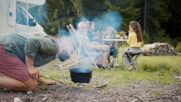 A mature man preparing barbecue at campsite outdoors, caravan family holiday trip.