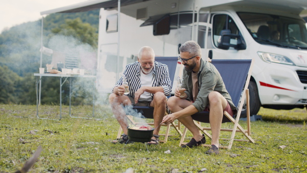 A mature man with senior father talking at campsite outdoors, barbecue on caravan holiday trip.