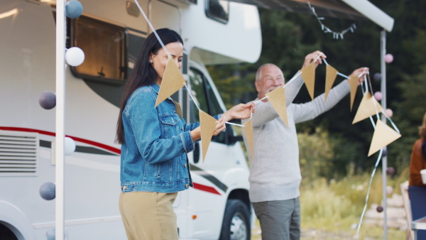 Happy multi-generation family preparing party by car outdoors in campsite, caravan holiday trip.