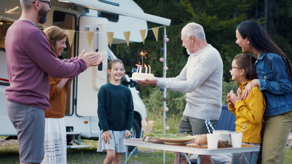 A multi-generation family celebrating birthday outdoors at campsite, caravan holiday trip.