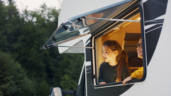 Happy small girls looking out through caravan window in the evening, a family holiday trip.