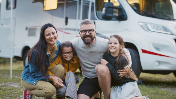 A family looking at camera outdoors at dusk, caravan holiday trip.