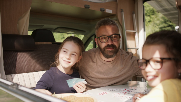 Happy small girls playing cards with father indoors in caravan, family holiday trip.