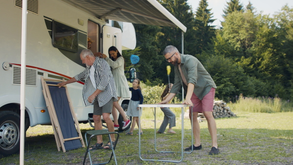 Happy multi-generation family unpacking and talking by car, caravan holiday trip.