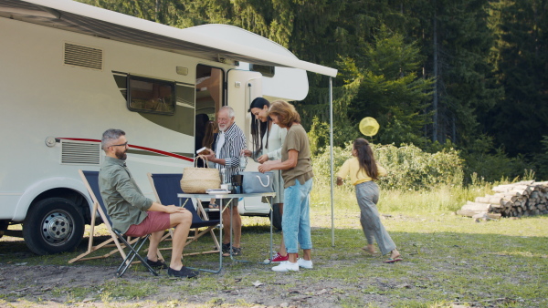 Happy multi-generation family unpacking and talking by car, caravan holiday trip.