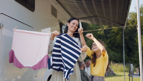 A mother with daughter hanging clothes by car outdoors in campsite, caravan family holiday trip.