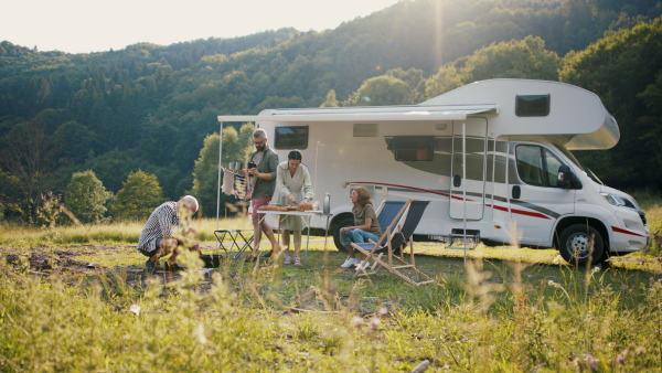 A multi-generation family preparing dinner outdoors by car, caravan holiday trip.