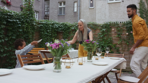 Young father with small son and his grandmother setting table for family dinner outdoors in back yard.