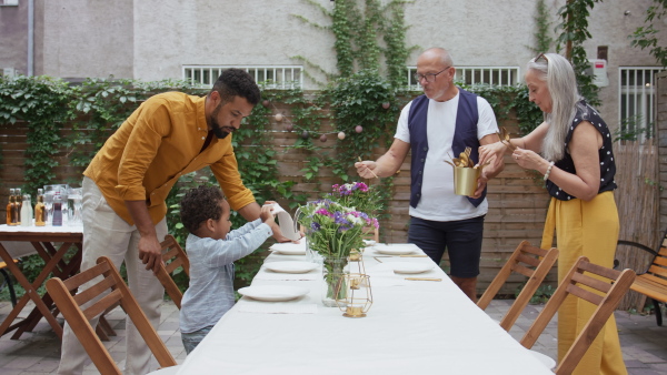 A little boy with his father and grandmother setting table for family dinner outdoors in back yard.