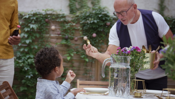 A father with small son and his grandfather setting table for family dinner outdoors in back yard.