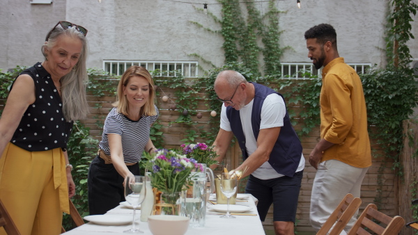 A young biracial couple with senior parents setting table for family dinner outdoors in back yard.