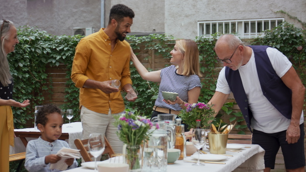 A young biracial couple with senior parents setting table for family dinner outdoors in back yard.