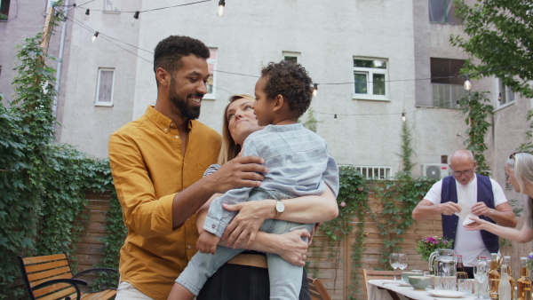 A happy biracial family with small son during family dinner with grandparents outdoors in garden.