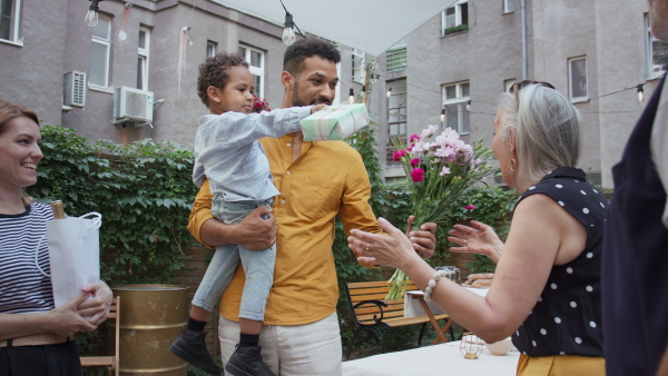 A multiracial little boy with parents giving birthday gift to his grandmother outdoors in back yard.