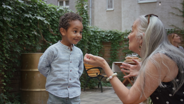 A multiracial little boy giving birthday gift to his senior grandmother outdoors in back yard.