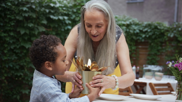 A grandmother with her multiracial grandson setting table for family dinner outdoors in back yard.