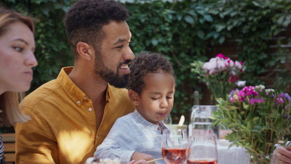 A young African American father with small son sitting at table and eating together during family dinner outdoors in back yard.