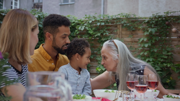 A young African American father with small son sitting at table and eating together during family dinner outdoors in back yard.