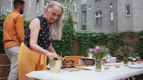 A senior woman setting table for family dinner outdoors in back yard.