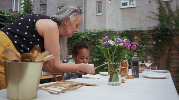 A grandmother with her multiracial grandson setting table for family dinner outdoors in back yard.